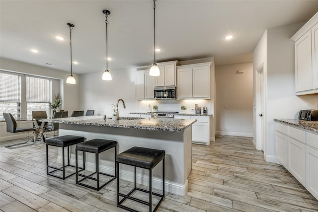 kitchen featuring white cabinetry, sink, stainless steel appliances, and an island with sink