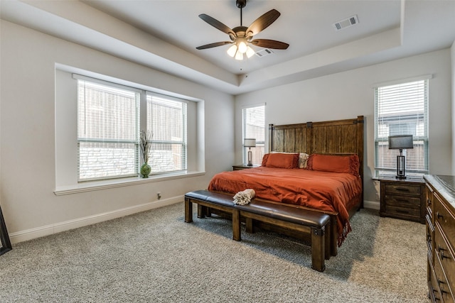 carpeted bedroom featuring multiple windows, a tray ceiling, and ceiling fan