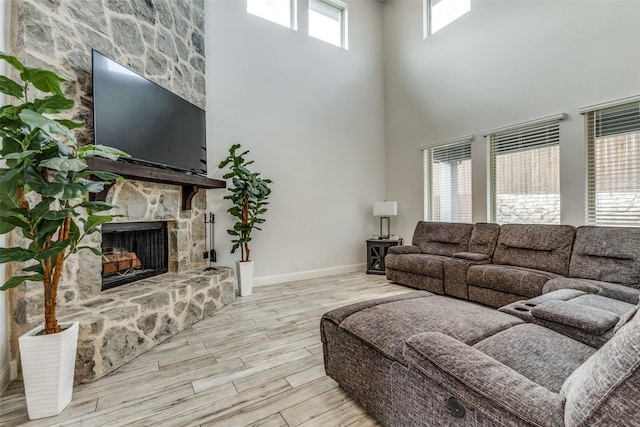 living room featuring a high ceiling, a stone fireplace, a wealth of natural light, and light hardwood / wood-style floors