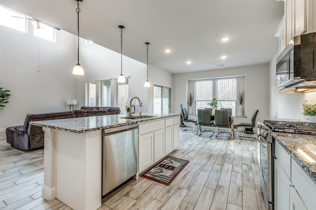 kitchen featuring appliances with stainless steel finishes, pendant lighting, an island with sink, sink, and white cabinets