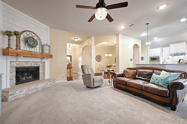 carpeted living room with arched walkways, visible vents, ceiling fan, a stone fireplace, and baseboards