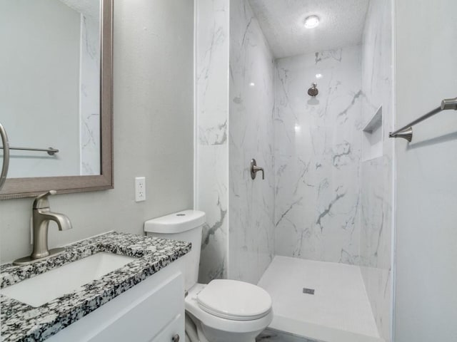 bathroom featuring a tile shower, vanity, toilet, and a textured ceiling