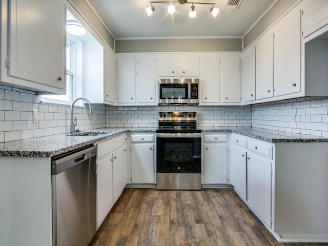 kitchen featuring appliances with stainless steel finishes, white cabinetry, sink, hardwood / wood-style flooring, and light stone counters