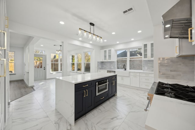 kitchen with range hood, oven, white cabinets, backsplash, and a center island