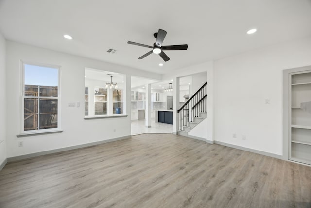 unfurnished living room with ceiling fan with notable chandelier and hardwood / wood-style floors