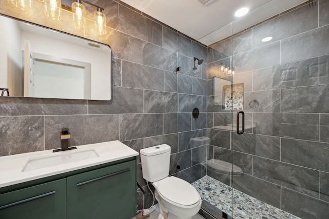 bathroom featuring a shower with door, tile walls, vanity, decorative backsplash, and toilet