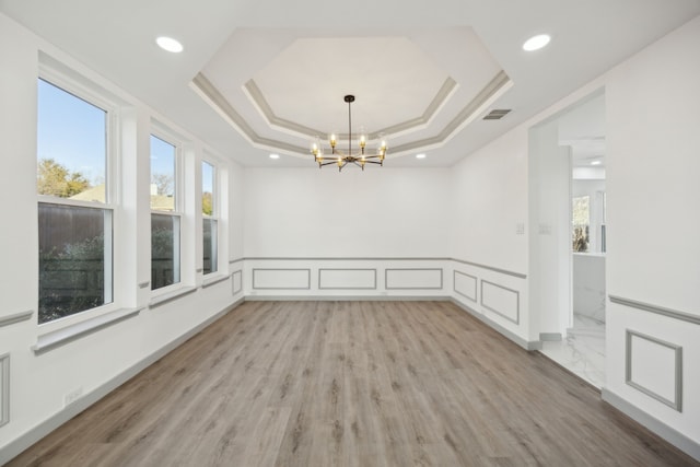 spare room featuring crown molding, a raised ceiling, a chandelier, and light wood-type flooring