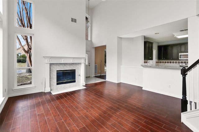 unfurnished living room with dark wood-type flooring, a towering ceiling, and a premium fireplace