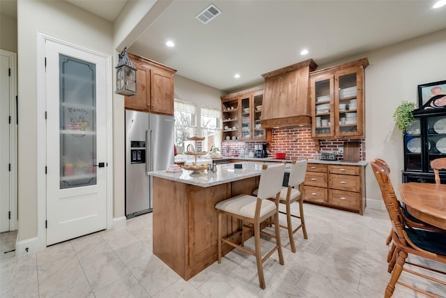 kitchen featuring a breakfast bar area, light stone counters, high quality fridge, a kitchen island, and decorative backsplash