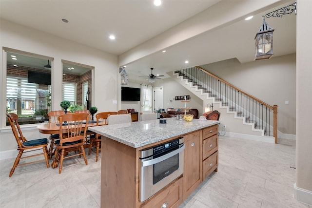 kitchen with light stone countertops, oven, ceiling fan, and a kitchen island