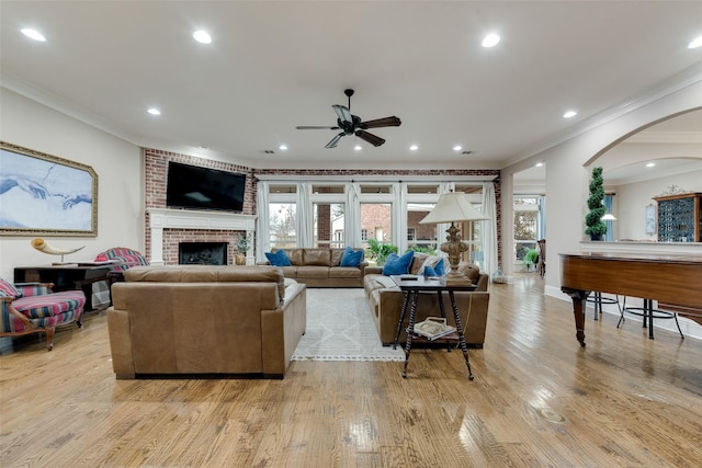 living room with ceiling fan, ornamental molding, a fireplace, and light hardwood / wood-style flooring