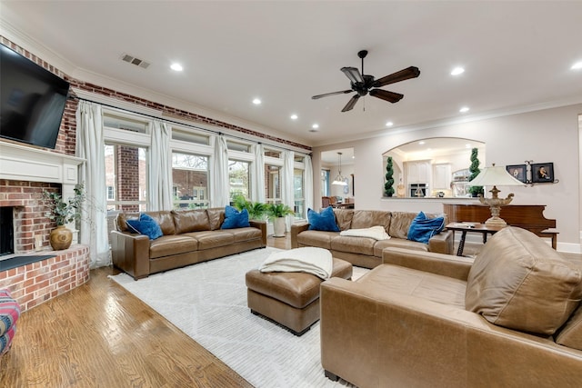 living room featuring ceiling fan, ornamental molding, a fireplace, and light hardwood / wood-style floors