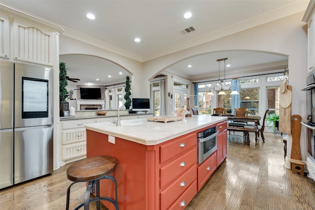 kitchen with sink, crown molding, light hardwood / wood-style flooring, stainless steel refrigerator, and a kitchen island with sink