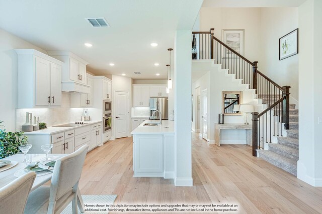 kitchen with white cabinetry, hanging light fixtures, stainless steel appliances, tasteful backsplash, and light wood-type flooring