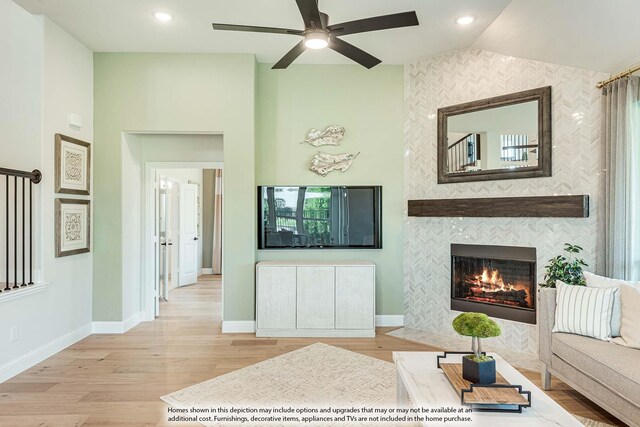 living room with ceiling fan, lofted ceiling, a tiled fireplace, and light hardwood / wood-style flooring