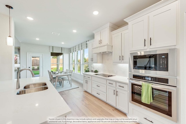 kitchen featuring pendant lighting, built in microwave, sink, white cabinets, and stainless steel oven