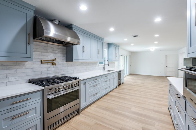 kitchen with sink, tasteful backsplash, light wood-type flooring, stainless steel appliances, and wall chimney range hood