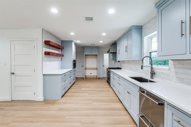 kitchen featuring sink, light wood-type flooring, stainless steel appliances, decorative backsplash, and wall chimney range hood