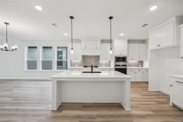 kitchen featuring built in microwave, sink, decorative light fixtures, an island with sink, and oven