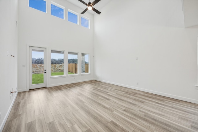 unfurnished living room with ceiling fan, light hardwood / wood-style flooring, and a high ceiling