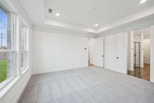 unfurnished bedroom featuring a raised ceiling, dark colored carpet, and multiple windows