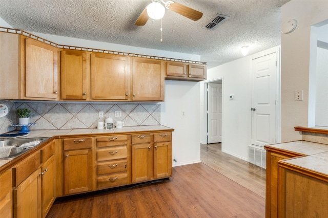 kitchen with a textured ceiling, tile counters, hardwood / wood-style flooring, ceiling fan, and decorative backsplash