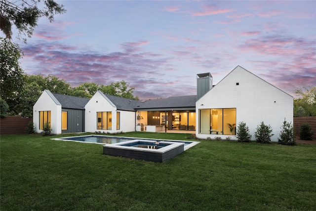 back house at dusk with a pool with hot tub and a lawn