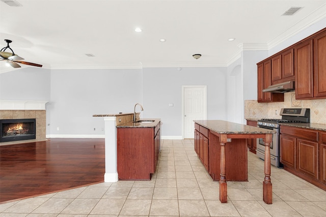 kitchen featuring sink, stainless steel range with gas cooktop, dark stone counters, and a center island with sink