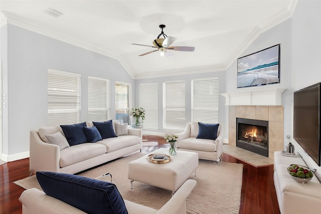 living room with vaulted ceiling, ornamental molding, dark hardwood / wood-style flooring, a tile fireplace, and ceiling fan