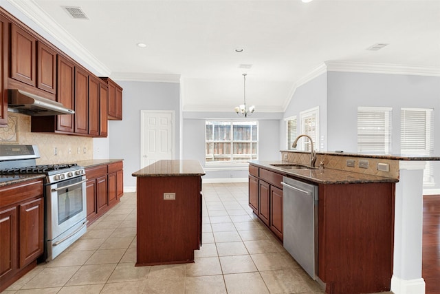 kitchen with stainless steel appliances, hanging light fixtures, sink, and a center island with sink