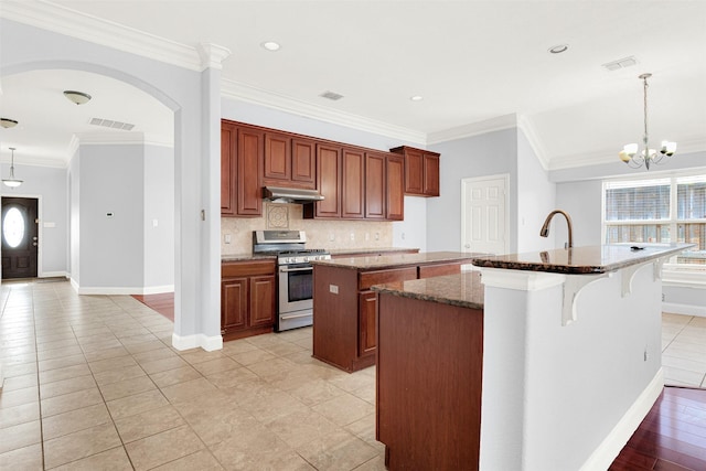 kitchen with a healthy amount of sunlight, hanging light fixtures, a center island with sink, and stainless steel gas range oven