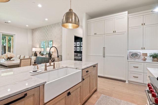 kitchen featuring light brown cabinetry, sink, hanging light fixtures, high end stainless steel range oven, and white cabinets