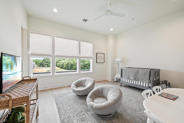 bedroom with a nursery area, ceiling fan, and light wood-type flooring