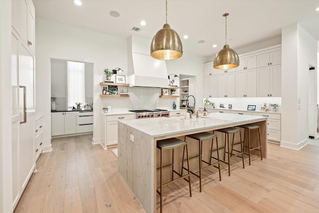 kitchen with decorative backsplash, custom exhaust hood, white cabinets, and a center island with sink