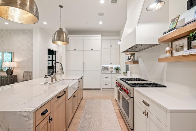 kitchen with pendant lighting, sink, white cabinetry, light stone counters, and range with two ovens