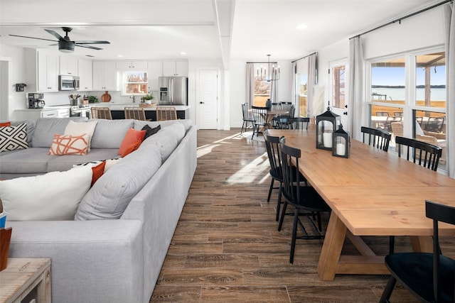 living room with dark wood-type flooring, a water view, and ceiling fan with notable chandelier