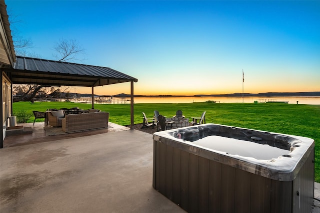 patio terrace at dusk featuring a hot tub, a gazebo, a water view, and a yard