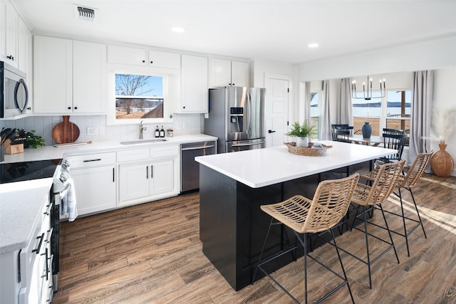 kitchen with a kitchen bar, sink, white cabinetry, appliances with stainless steel finishes, and a kitchen island