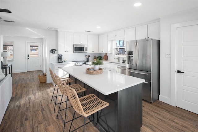 kitchen featuring dark wood-type flooring, a breakfast bar, stainless steel appliances, white cabinets, and a kitchen island