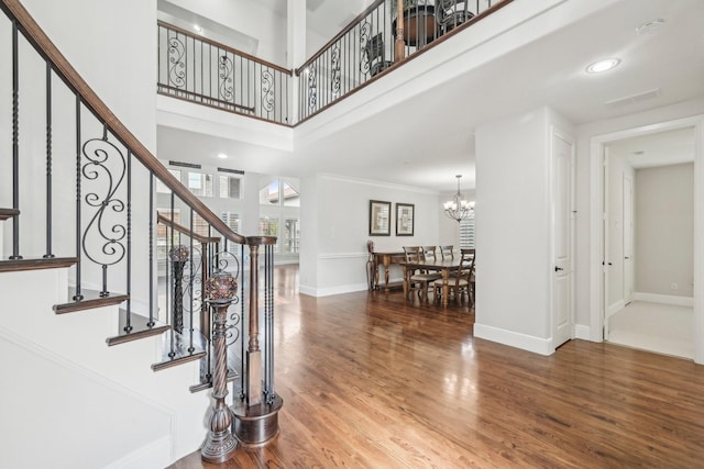 foyer entrance featuring hardwood / wood-style flooring, ornamental molding, an inviting chandelier, and a high ceiling