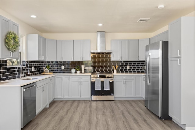 kitchen with tasteful backsplash, sink, stainless steel appliances, wall chimney range hood, and light wood-type flooring