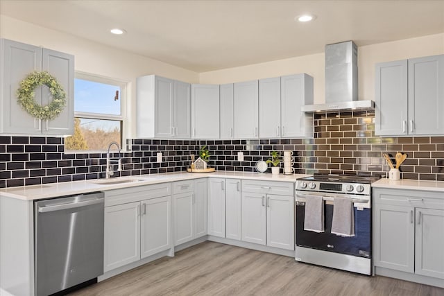 kitchen featuring appliances with stainless steel finishes, tasteful backsplash, sink, wall chimney exhaust hood, and light hardwood / wood-style flooring