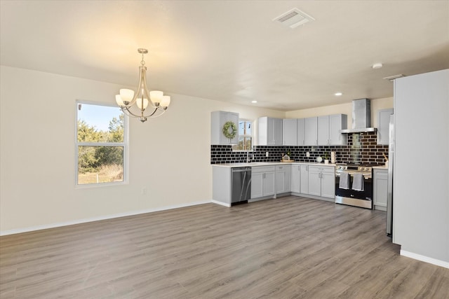 kitchen with appliances with stainless steel finishes, white cabinetry, decorative light fixtures, wall chimney exhaust hood, and light wood-type flooring