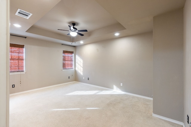 empty room featuring a tray ceiling, light colored carpet, and ceiling fan