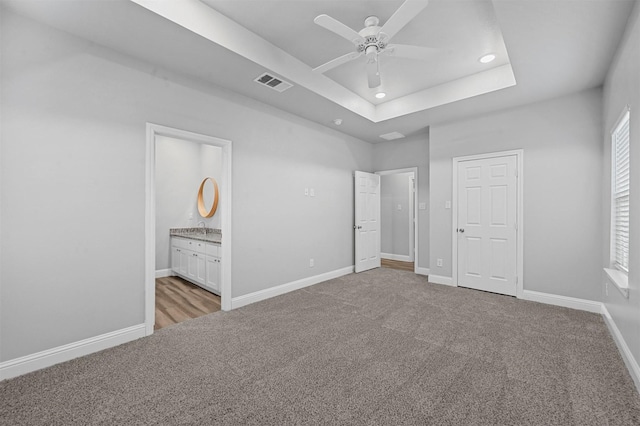 unfurnished bedroom featuring connected bathroom, a tray ceiling, light colored carpet, and ceiling fan