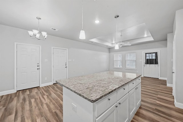 kitchen featuring pendant lighting, hardwood / wood-style flooring, a center island, a tray ceiling, and white cabinets