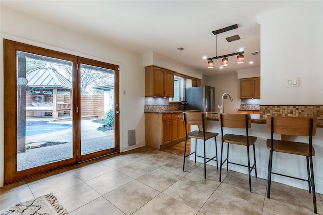 kitchen with light tile patterned flooring, high end fridge, tasteful backsplash, a kitchen breakfast bar, and pendant lighting