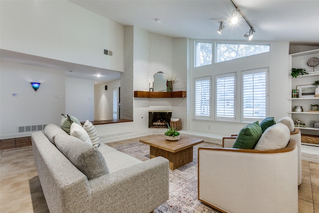 living room featuring a brick fireplace, light tile patterned floors, high vaulted ceiling, and rail lighting