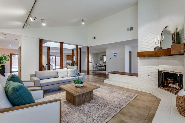 living room featuring rail lighting, a brick fireplace, light tile patterned floors, and high vaulted ceiling