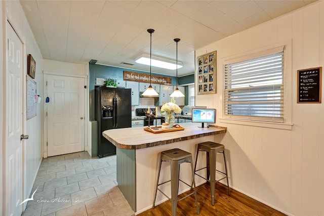 kitchen with a kitchen breakfast bar, kitchen peninsula, hanging light fixtures, and black appliances